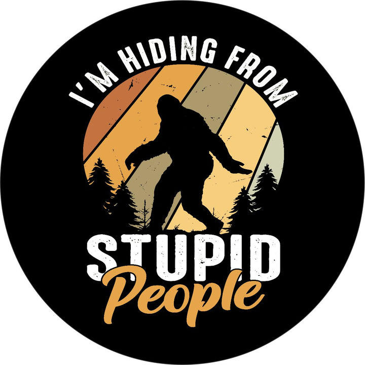 Vibrant and high quality vinyl spare tire cover made from orange and red earth tones with a silhouette of sasquatch and the saying, I'm hiding from stupid people