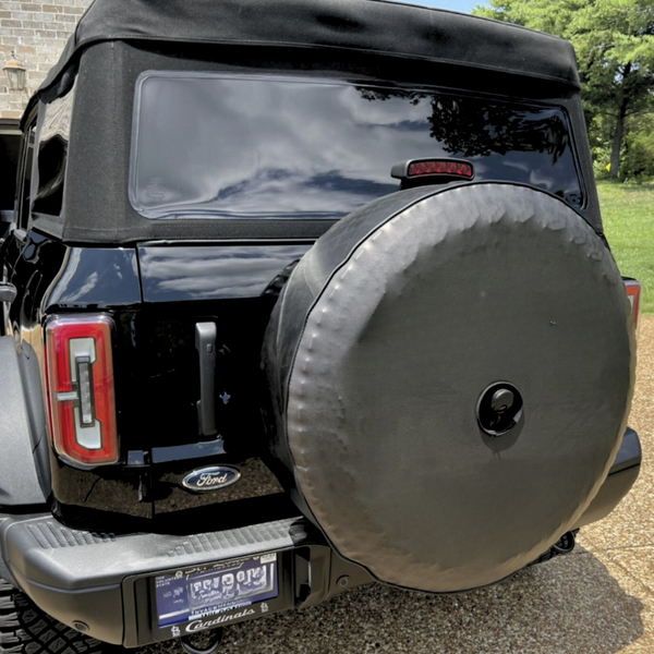 Tightly fit vinyl all solid black spare tire cover with a back up camera port hole on a black Ford Bronco soft top