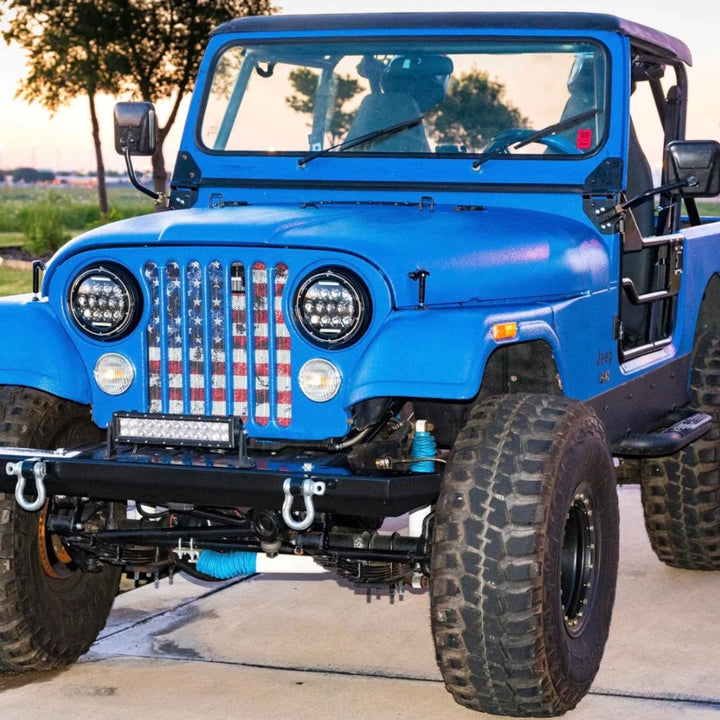 Blue vintage Jeep Wrangler with two doors and top off the back displaying a grille insert of a full color red white and blue American flag with rustic detail 