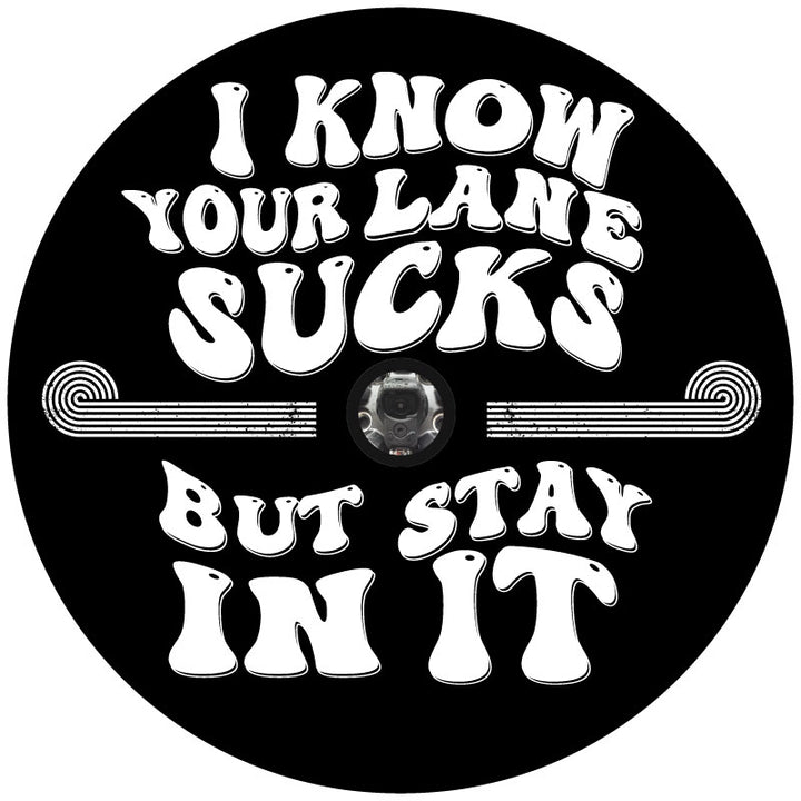 Mockup graphic design for a black vinyl funny spare tire cover that says, "I know your lane sucks but stay in it" in big, bold, retro designed lettering with a hole in the middle to accommodate a backup camera. 