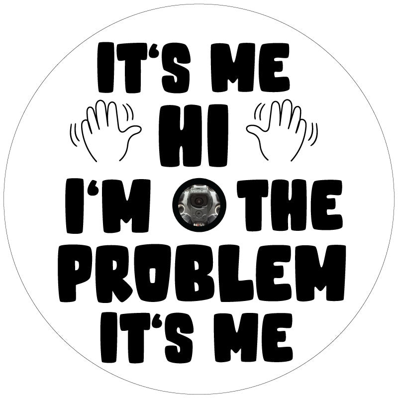 White vinyl spare tire cover with black text of the Taylor Swift song lyrics, It's Me. Hi. I'm The Problem It's Me and two hands waving and a backup camera hole to accommodate spare tire covers that have a camera in the center.