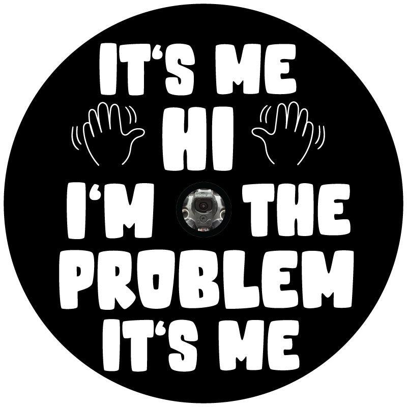 Black vinyl spare tire cover with white text of the Taylor Swift song lyrics, It's Me. Hi. I'm The Problem It's Me and two hands waving and a backup camera hole to accommodate spare tire covers that have a camera in the center.