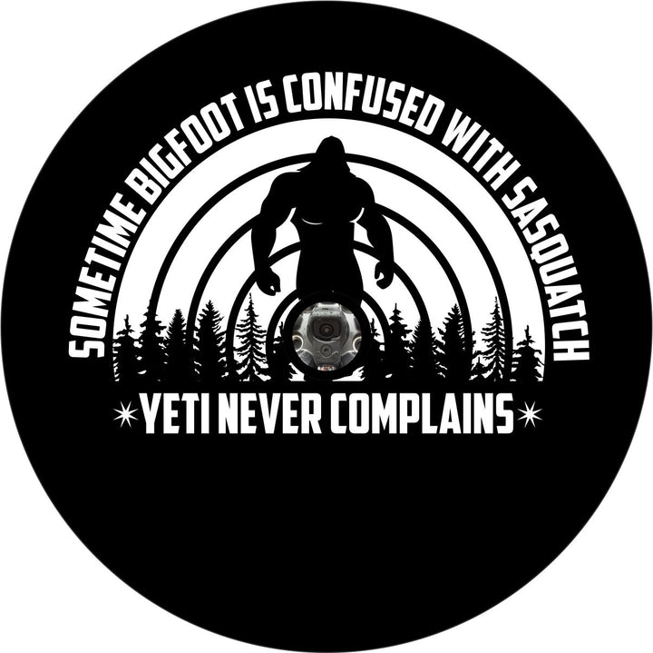 Mockup design of a black vinyl spare tire cover with a funny saying, "Sometime bigfoot is confused with Sasquatch, Yeti never complains" and a silhouette of sasquatch in the background. The spare tire cover design is for a backup camera and has a center hole