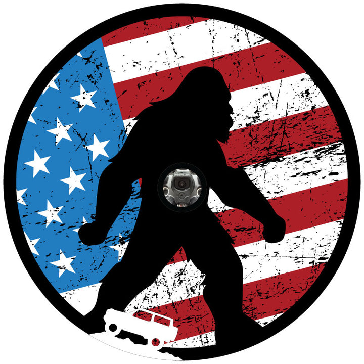 Mockup spare tire cover design for a soft black vinyl spare wheel, design is a rustic American flag red, white, and blue background with a black silhouette of Sasquatch bigfoot and a small white Ford Bronco icon on the bottom plus a center section to accommodate covers for spare wheels with backup cameras.