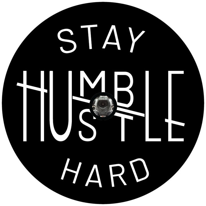 A spare tire cover design for a Jeep, Bronco, RV, camper, van, etc. with a unique design play on the words stay humble hustle hard with white text meant for black vinyl and a backup camera hole.