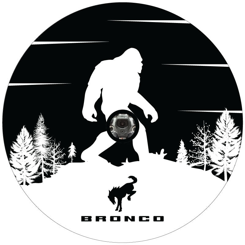 Black vinyl spare tire cover with a white and black silhouette of a bigfoot sasquatch and a Ford Bronco logo design custom made for a Ford Bronco Sasquatch spare tire with a backup camera.