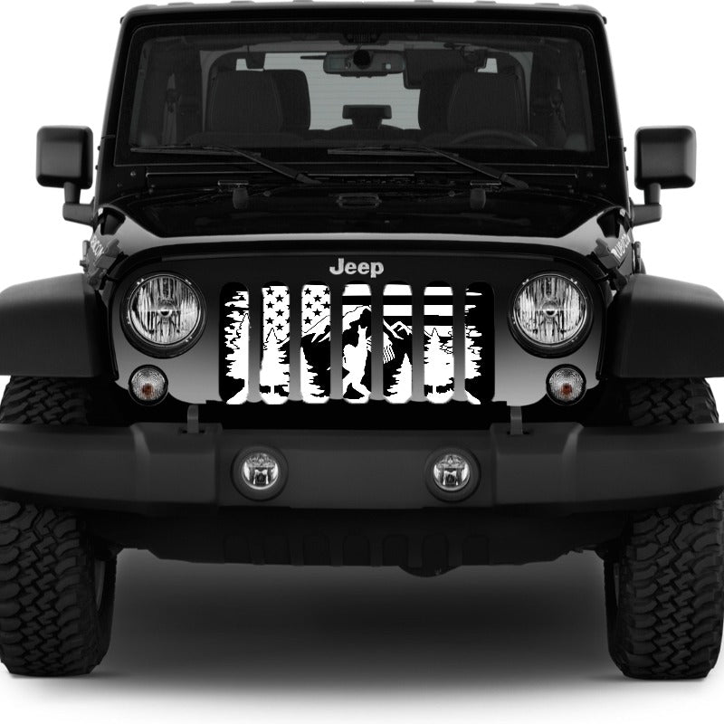 Front end of a black Jeep Wrangler showing a Jeep grille insert design of an American flag background, mountains and a forest, with Bigfoot or Sasquatch walking by showing a peace sign holding the American flag.