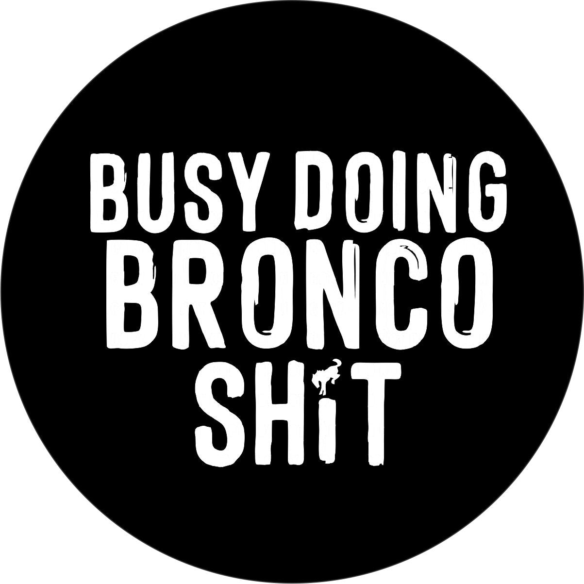 Black vinyl spare tire cover that boldy says "busy doing Bronco shit" and the dot in the I is a Bronco horse icon.