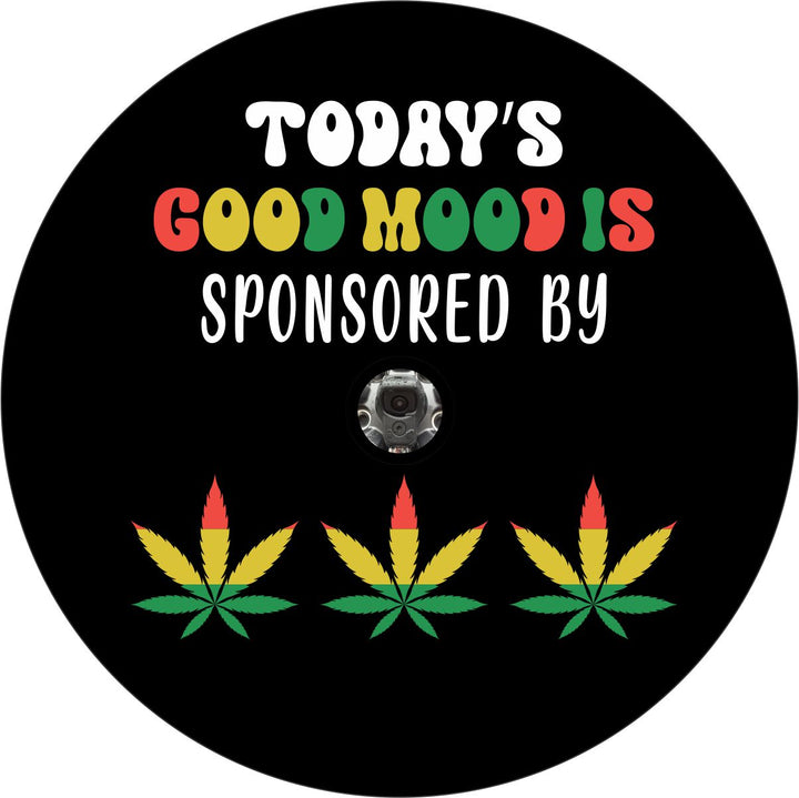 Spare tire cover with the saying "today's mood is sponsored by" and the shape of cannabis leaves colored with rasta red, yellow, green colors plus a hole for a back back up camera model spare wheels.