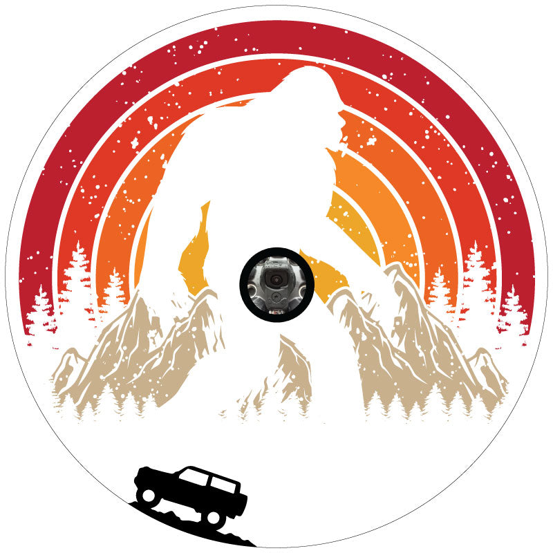 A retro vintage spare tire cover design with Sasquatch or bigfoot walking through the mountains and the silhouette of a Ford Bronco driving.  Designed for a white vinyl spare tire cover and a back up camera